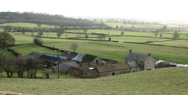 A rural landscape with a stone farm, green fields, and a distant hill.