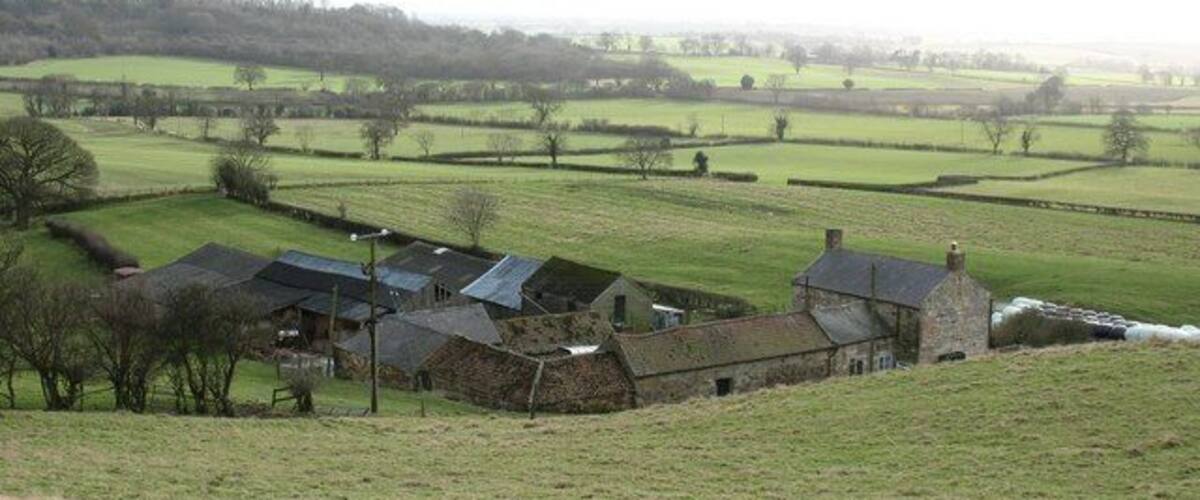 A rural landscape with a stone farm, green fields, and a distant hill.