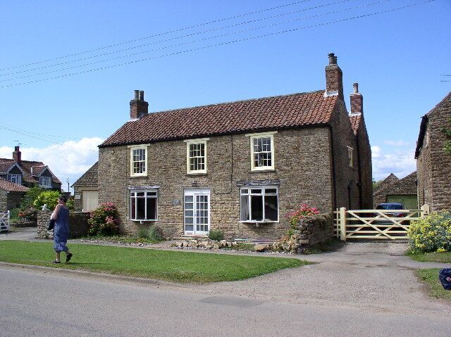 A stone house with a tiled roof, a wooden gate, and a grassy lawn.