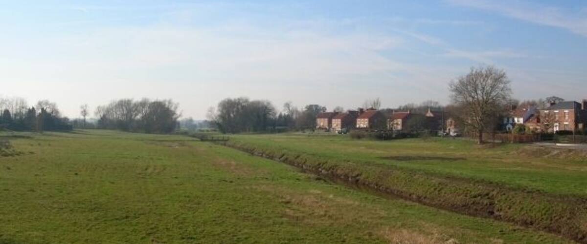 A rural landscape with green fields, a stone wall, and houses in the background.