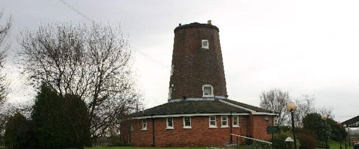 A brick building with a tower, a grassy field, and a street lamp.