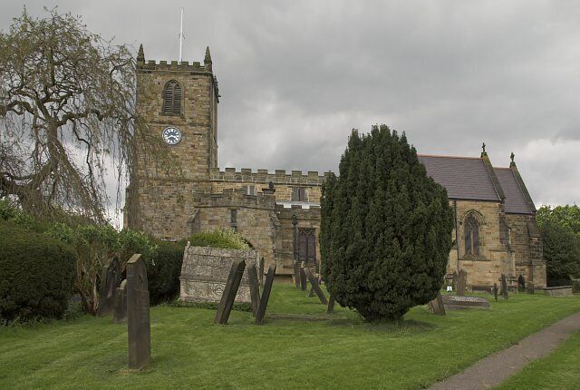 A historic stone church with a tall tower and a large tree in the foreground.