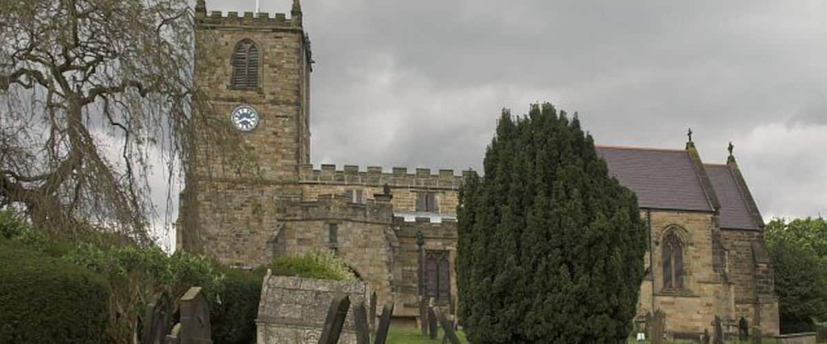 A historic stone church with a tall tower and a large tree in the foreground.
