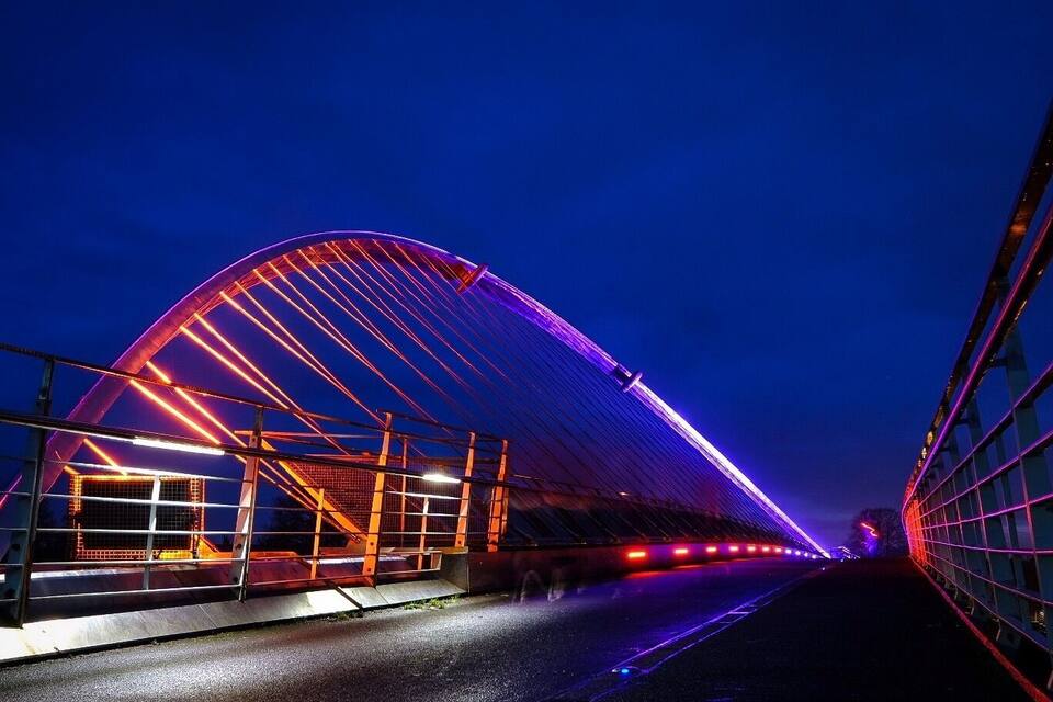 A bridge at night with illuminated red and purple lights.