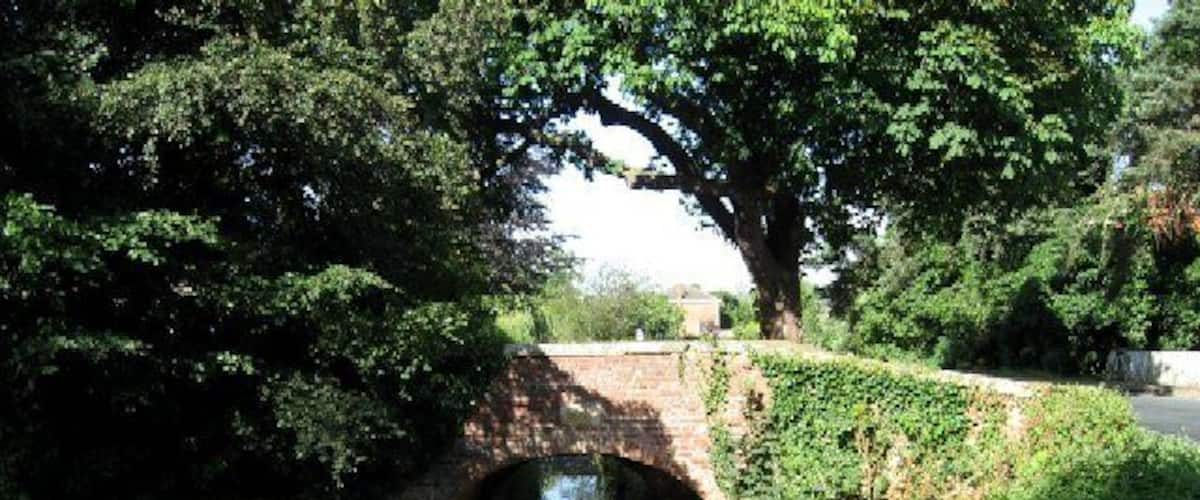 A narrow waterway under a stone bridge surrounded by lush greenery.