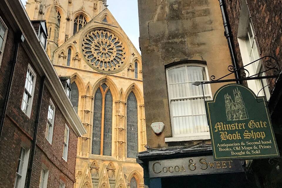 A historic building with a large rose window and a bookshop named 'Minster Gate Book Shop' below it.