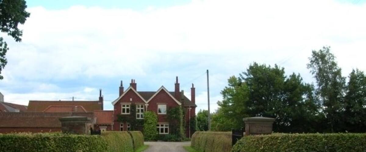 A gravel driveway leading to a red brick house with a white window and a chimney.