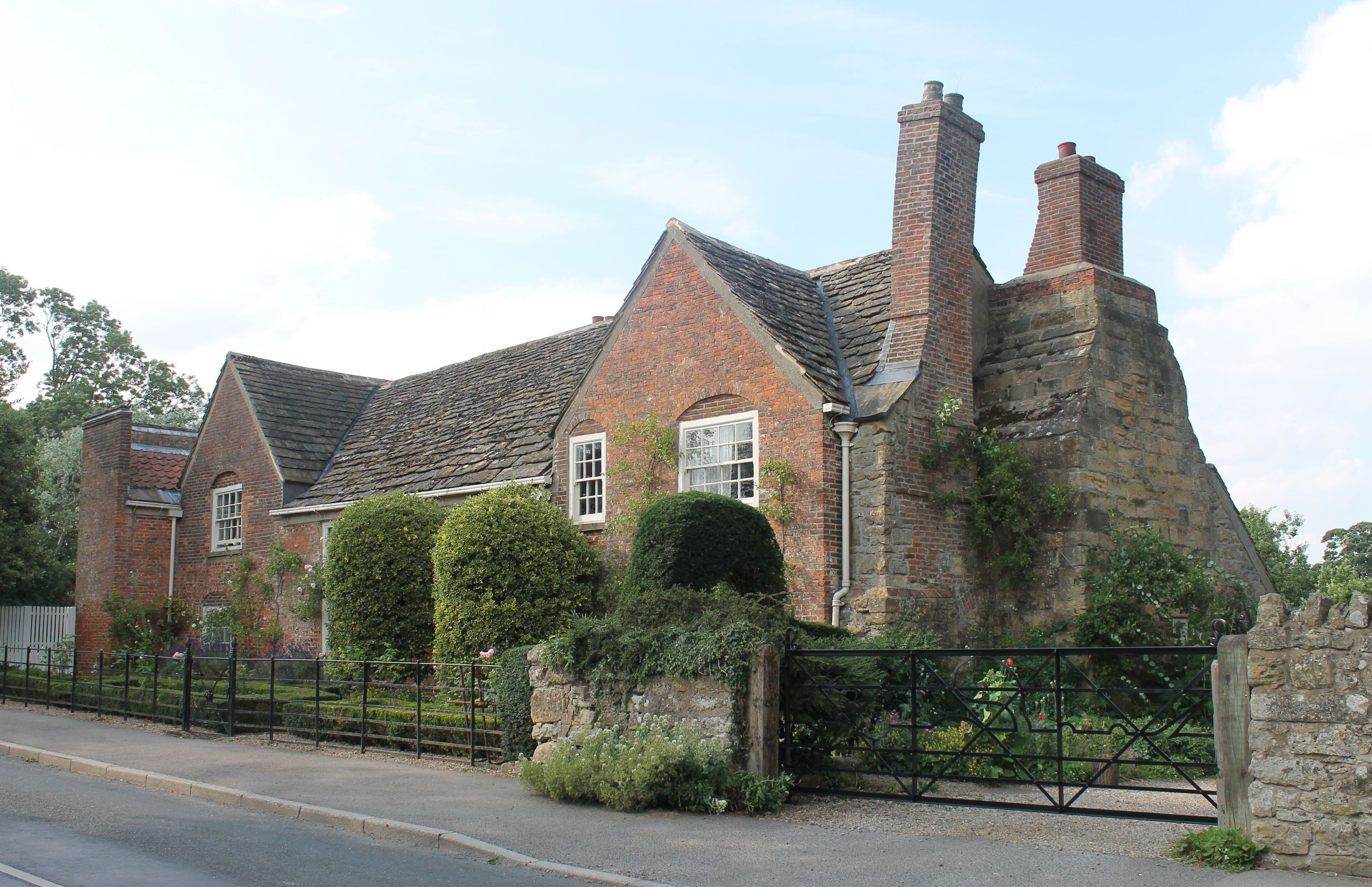 A historic brick house with a stone wall and a metal gate.
