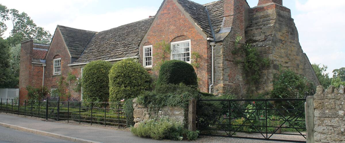 A historic brick house with a stone wall and a metal gate.