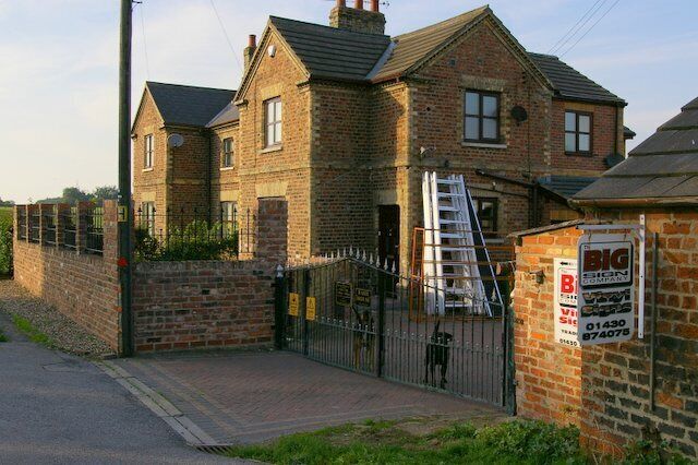 A brick house with a gated driveway and a ladder leading to the second floor.