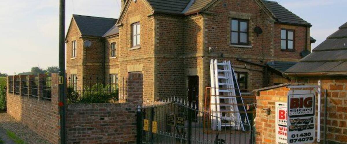 A brick house with a gated driveway and a ladder leading to the second floor.
