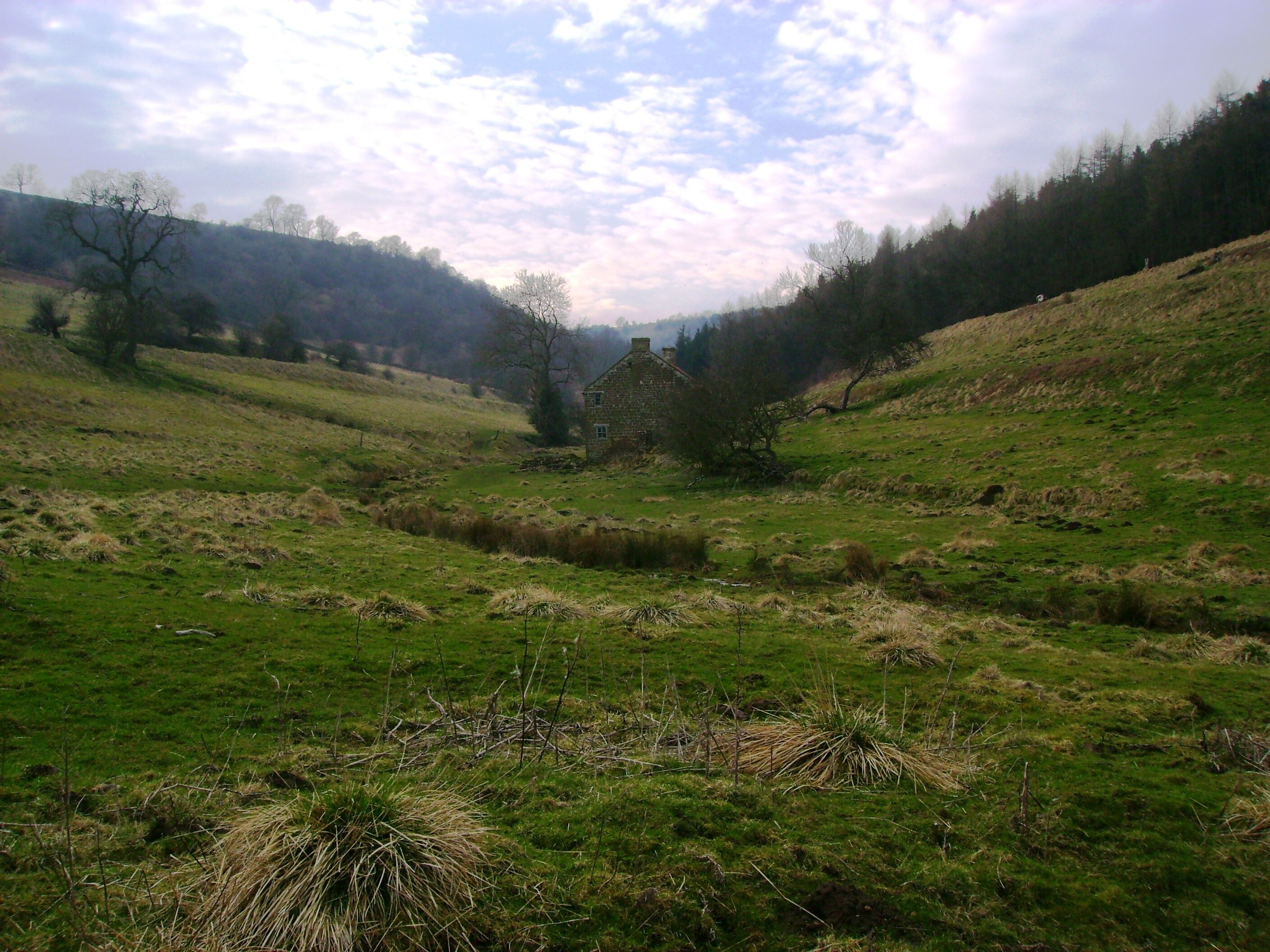 A stone house in a valley surrounded by hills and trees.