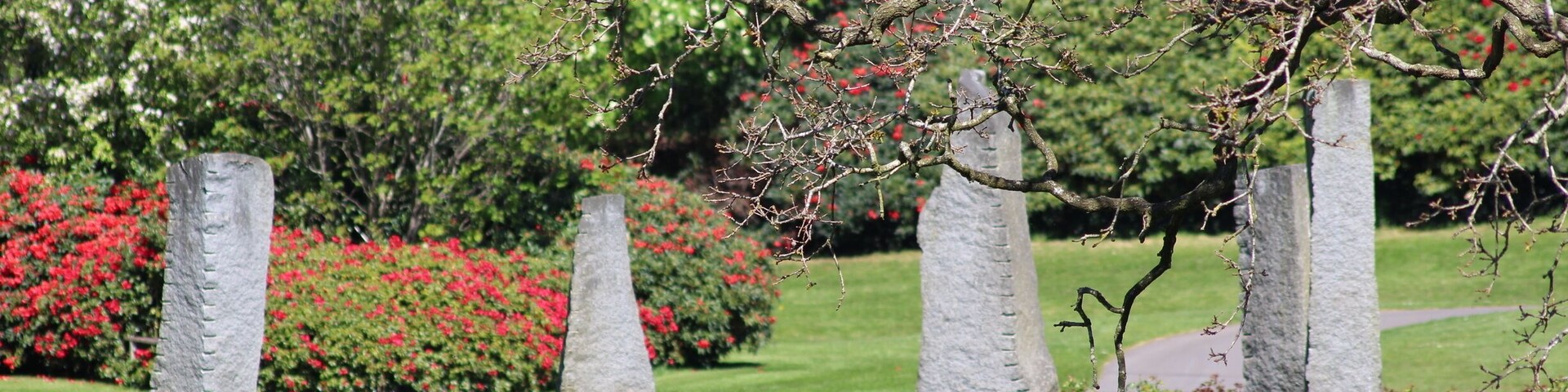 Ein Garten mit Steinpfeilern, grünem Gras und roten Blumen.
