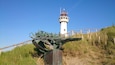 Un phare, une sculpture en métal et une clôture en bois.