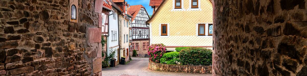 A cobblestone street with a stone archway, traditional half-timbered houses, and a clear blue sky.