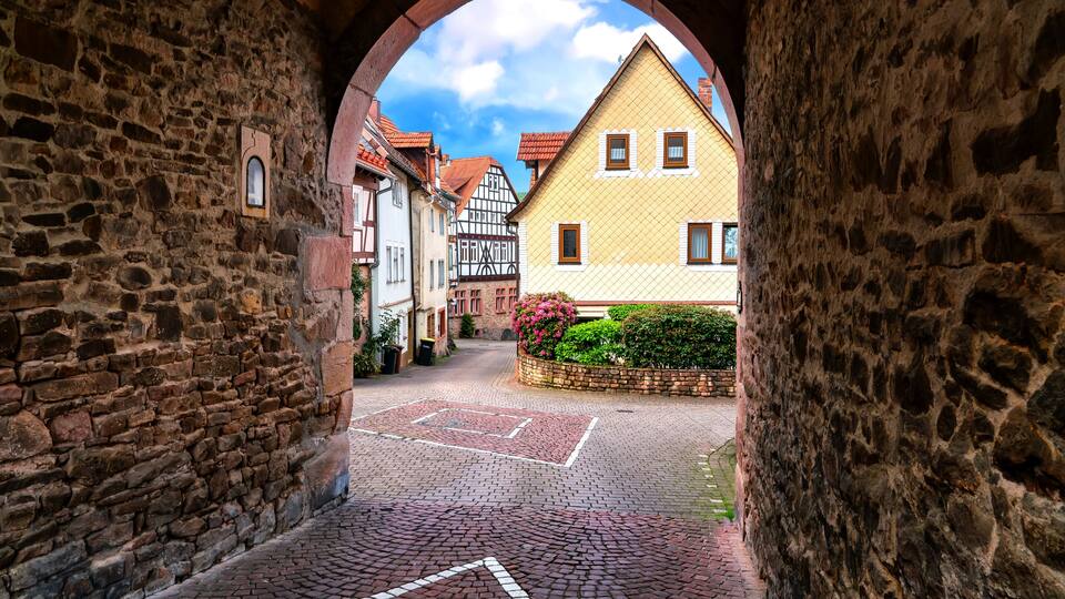 A cobblestone street with a stone archway, traditional half-timbered houses, and a clear blue sky.