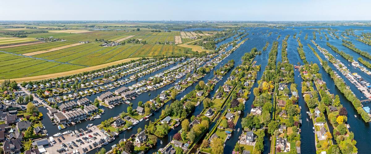 An aerial view of a river with numerous docks and boats, surrounded by residential areas and green fields.