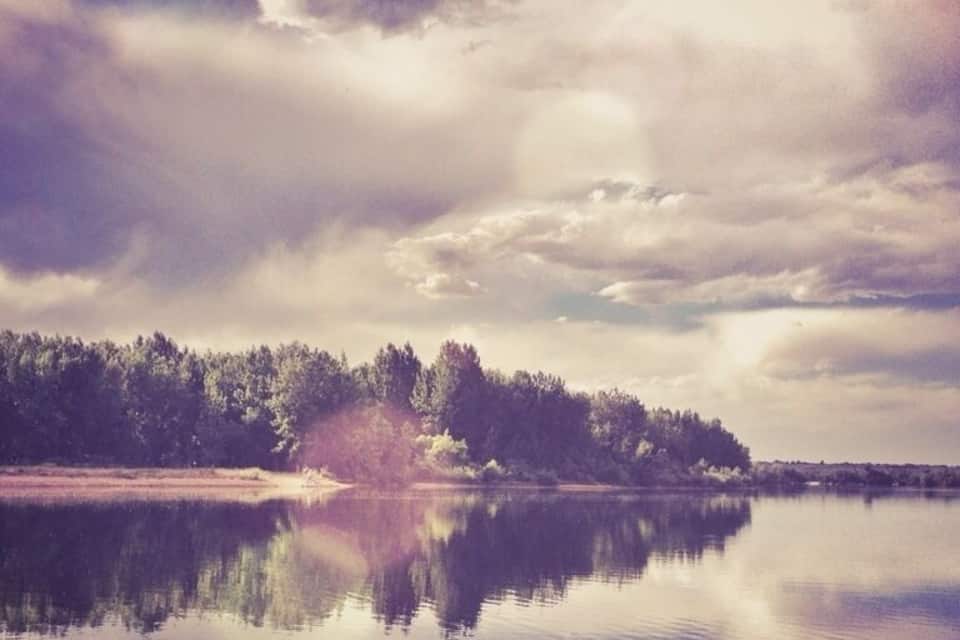 Um lago tranquilo com margens arborizadas e céu nublado.