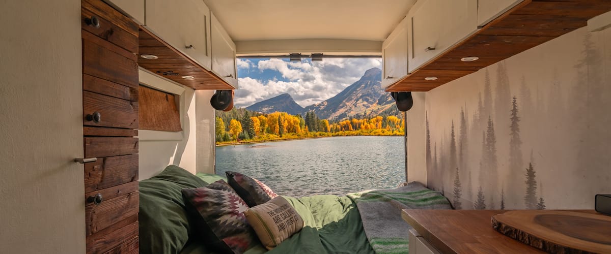 Vanlife Campervan Bed in Wilderness Colorado Mountain Aspen Tree Lake in Autumn Fall Foliage. Green Bedding and Wooden Details with Back Door Open..