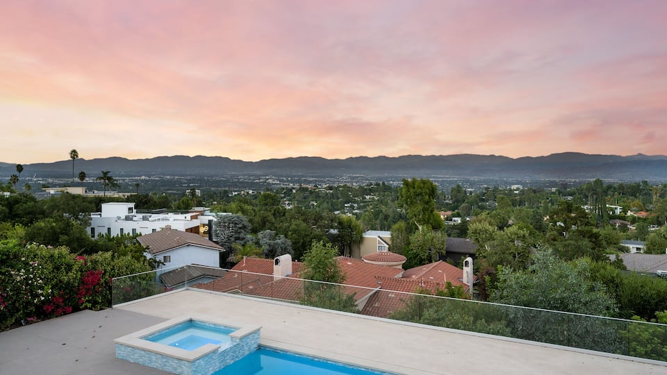 A residential area with a swimming pool, houses, and a mountainous landscape in the background.