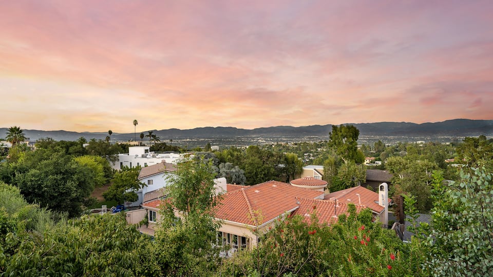 A residential area with houses, trees, and a distant mountain range under a sunset sky.