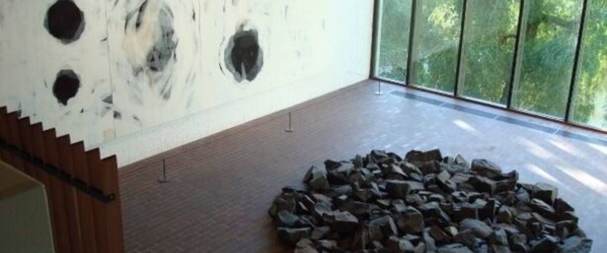 A modern art gallery with abstract paintings on the wall and a circular arrangement of rocks on the floor.
