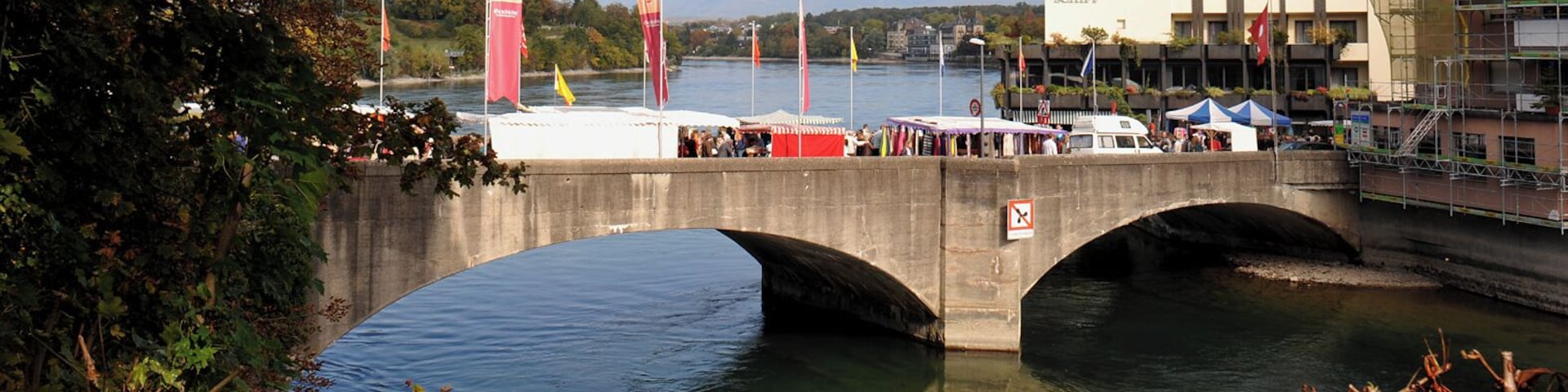 Old bridge over the Rhine by Robert Maillart in Rheinfelden, built 1912; Aargau, Switzerland and Baden-Württemberg, Germany. Flags on the occasion of the Rheinfelden autumn market. Narrow part of the river on the Swiss side.