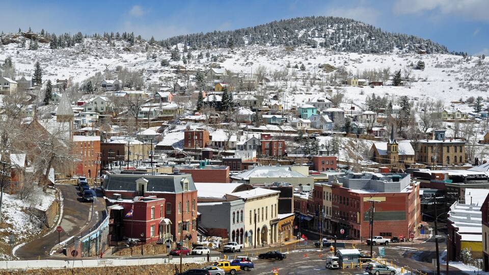 A snow-covered town with buildings, a street, and a hill in the background.