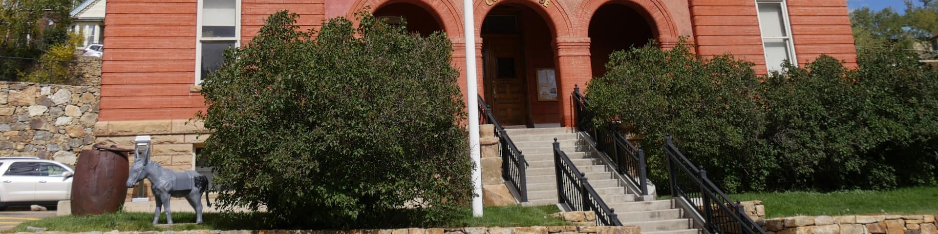 A red brick courthouse with a flagpole, an American flag, and a state flag.