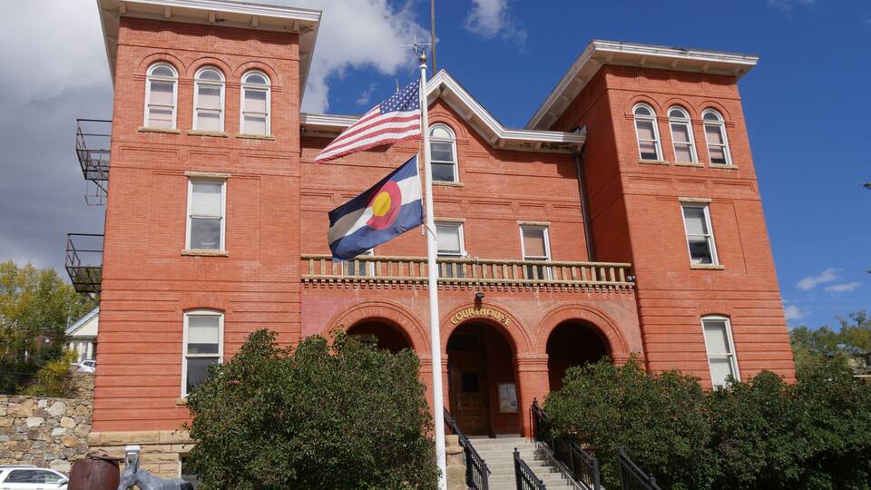 A red brick courthouse with a flagpole, an American flag, and a state flag.