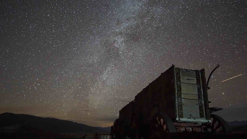 A starry night sky with a vintage truck parked in a desert landscape.