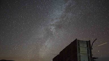 Céu estrelado à noite com uma caminhonete antiga estacionada em uma paisagem desértica.