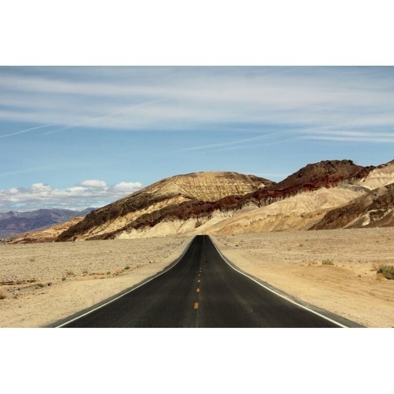 A road through a desert landscape with layered rock formations.