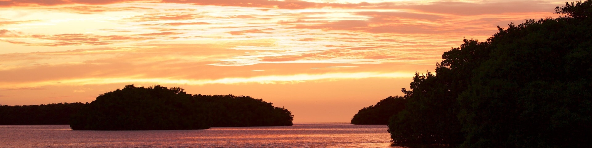 A sunset over a body of water with two islands silhouetted against the sky.