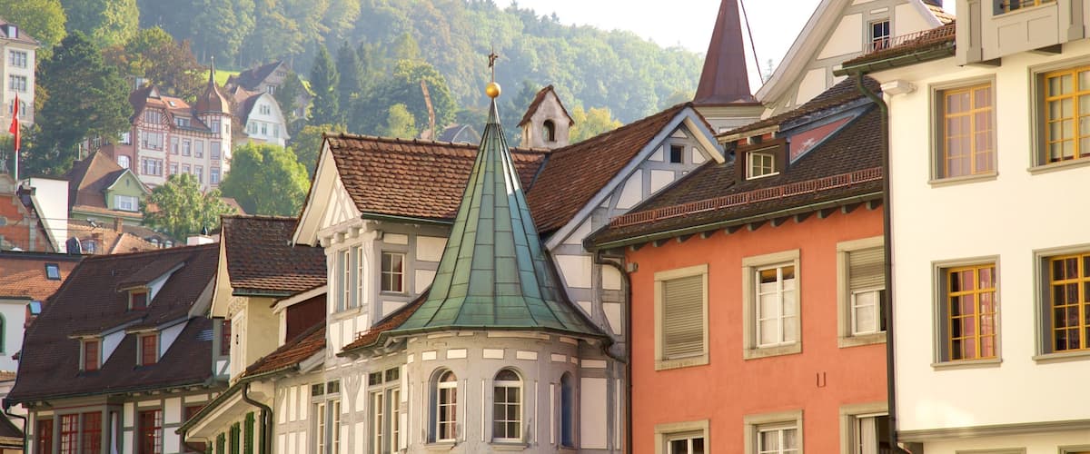 A historic European town with colorful buildings, a prominent church with a green spire, and a restaurant named "AM CALLU".