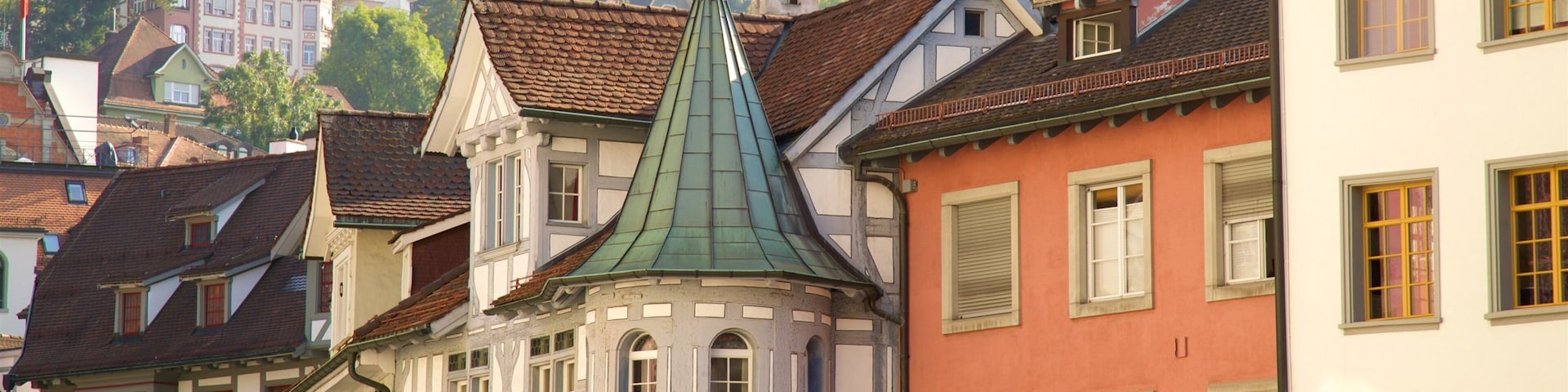 A historic European town with colorful buildings, a prominent church with a green spire, and a restaurant named "AM CALLU".