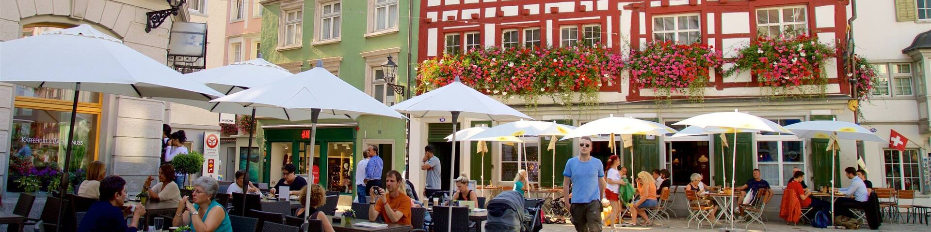 A European street with colorful half-timbered buildings, outdoor cafes, and people dining.
