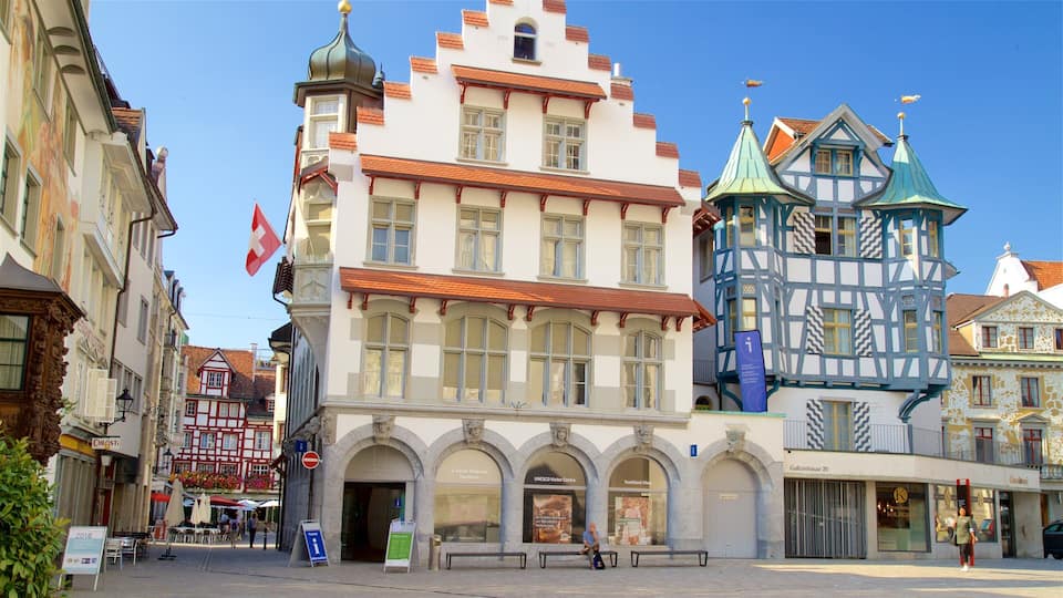 A historic European town square with traditional architecture, including a building with a green roof and a half-timbered structure.
