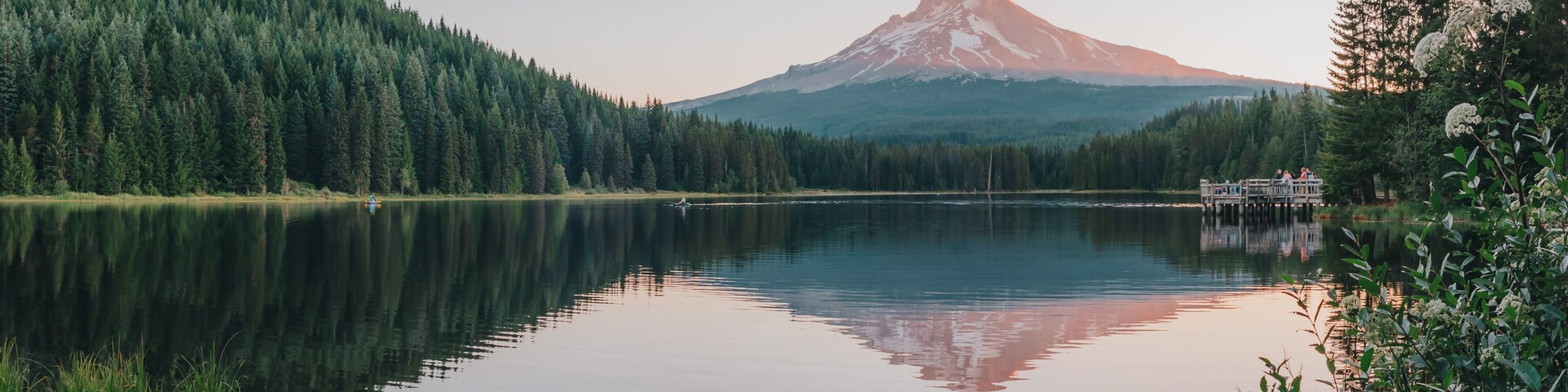 Un lago tranquilo con una montaña boscosa al fondo.