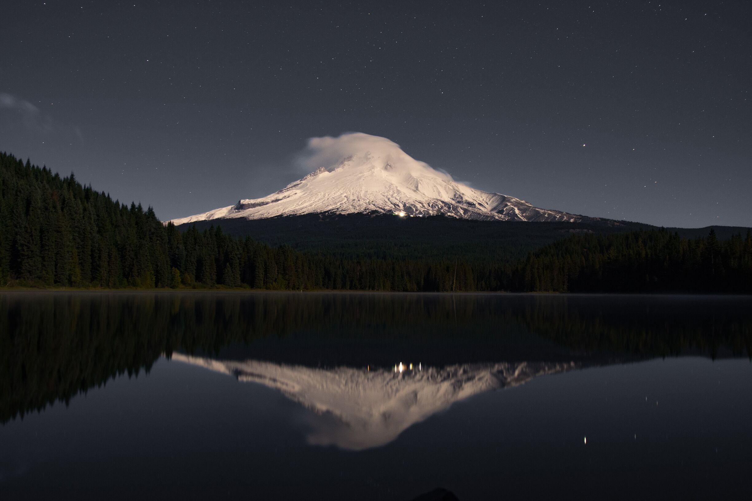 A snow-capped mountain reflected in a calm lake at night.