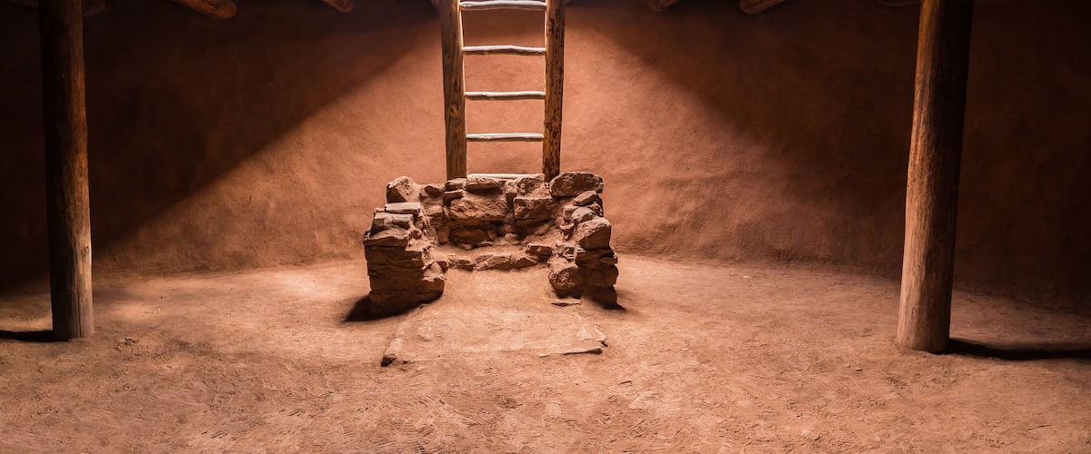 A stone structure with a wooden ladder in a dimly lit room with wooden beams on the ceiling.