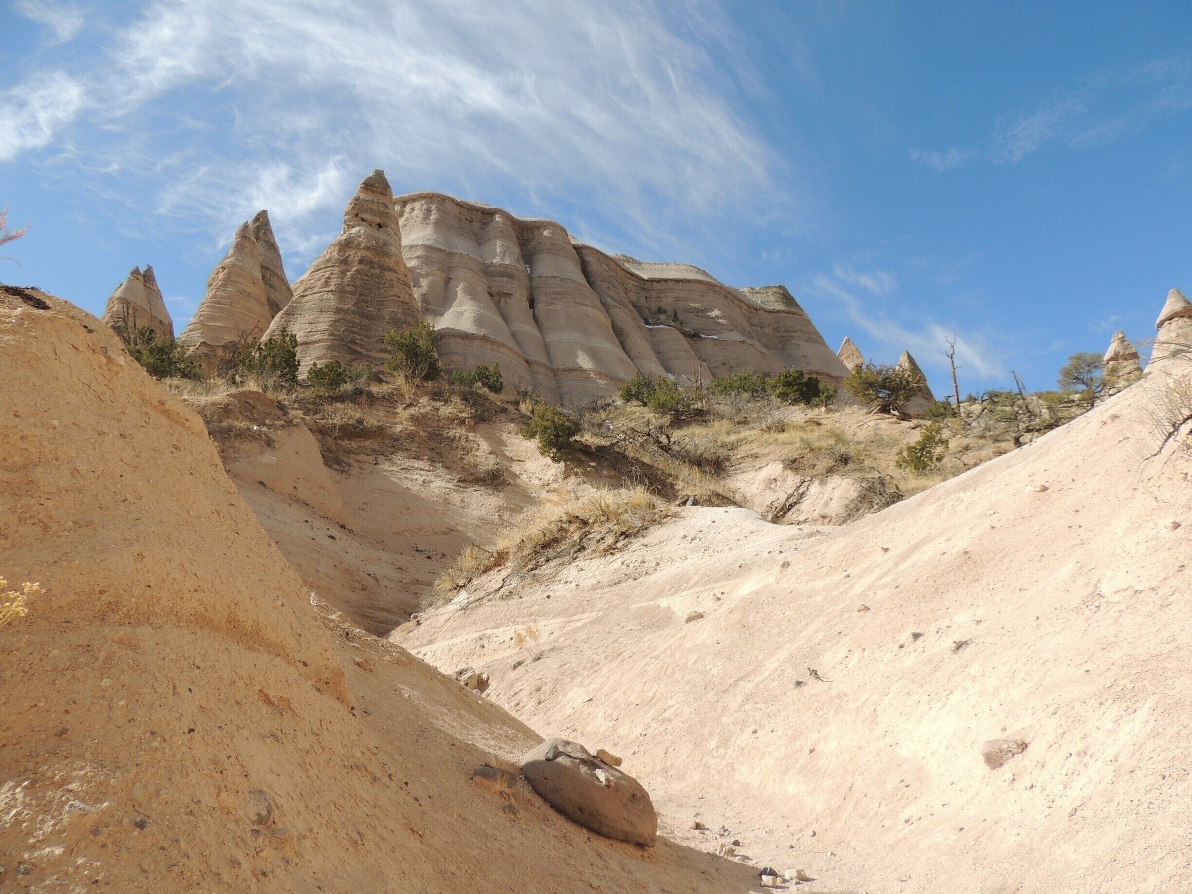 New Mexico’s stunning Kasha-Katuwe Tent Rock formations are the product of volcanic eruptions 6 to 7 million years ago.  Many of the pumice, ash and tuff deposits are over 1,000 feet thick.  Tremendous explosions from the Jemez volcanic field spewed pyroclasts (rock fragments), while searing hot gases blasted down slopes in an incandescent avalanche called a “pyroclastic flow.” 

 Over time, wind and water cut into these deposits creating canyons and arroyos, scooping holes in the rock and contouring the ends of small, inward ravines into smooth semi-circles.  
Two hiking trails (the Cave Loop Trail and the Canyon Trail) allow visitors amazing access to this National Monument.  We hiked the tougher Canyon Trail, a 1.5 mile trek up a narrow canyon involving a 630-foot climb to the mesa top, driven by the promise of fantastic views of the Sangre de Cristo, Jemez, and Sandia mountains, as well as the Rio Grande Valley.   We were not disappointed.  

Be sure to arrive early in the day (the monument opens at 8 am during winter months, 7 am during the summer) to avoid the crowds and the heat.   Bring plenty of water; the monument has no concessions, but does offer the basics in terms of facilities.  The nominal $5 fee per vehicle is returned to the site for monitoring, maintenance, and improvements.

See more pictures and commentary via my blog at http://www.aplacecalledroam.com/home/hiking-the-stunning-kasha-katuwe-tent-rocks-national-monument .