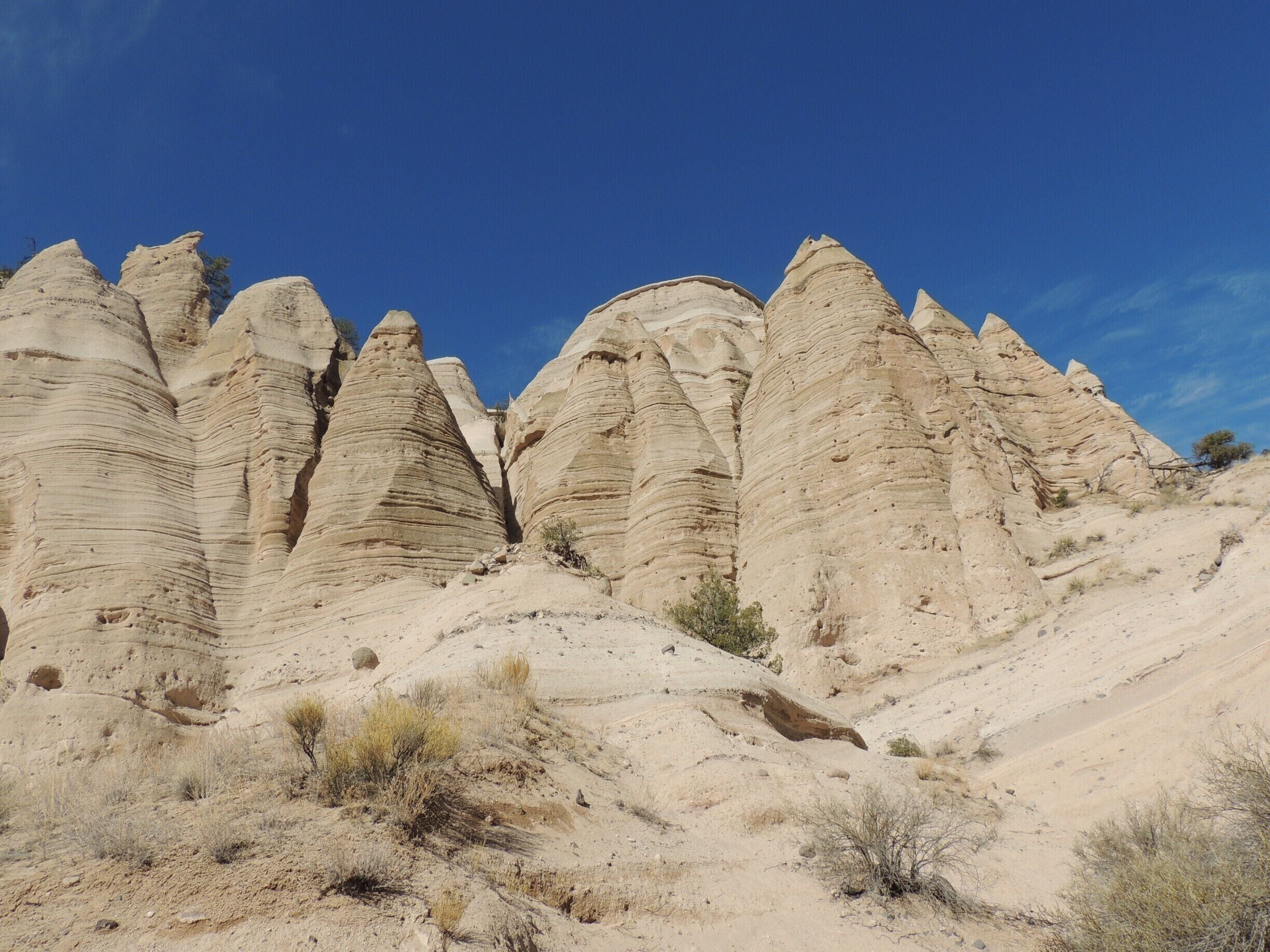 New Mexico’s stunning Kasha-Katuwe Tent Rock formations are the product of volcanic eruptions 6 to 7 million years ago.  Many of the pumice, ash and tuff deposits are over 1,000 feet thick.  Tremendous explosions from the Jemez volcanic field spewed pyroclasts (rock fragments), while searing hot gases blasted down slopes in an incandescent avalanche called a “pyroclastic flow.” 

 Over time, wind and water cut into these deposits creating canyons and arroyos, scooping holes in the rock and contouring the ends of small, inward ravines into smooth semi-circles.  

Two hiking trails (the Cave Loop Trail and the Canyon Trail) allow visitors amazing access to this National Monument.  We hiked the tougher Canyon Trail, a 1.5 mile trek up a narrow canyon involving a 630-foot climb to the mesa top, driven by the promise of fantastic views of the Sangre de Cristo, Jemez, and Sandia mountains, as well as the Rio Grande Valley.   We were not disappointed.  

Be sure to arrive early in the day (the monument opens at 8 am during winter months, 7 am during the summer) to avoid the crowds and the heat.   Bring plenty of water; the monument has no concessions, but does offer the basics in terms of facilities.  The nominal $5 fee per vehicle is returned to the site for monitoring, maintenance, and improvements.

See more pictures and commentary via my blog at http://www.aplacecalledroam.com/home/hiking-the-stunning-kasha-katuwe-tent-rocks-national-monument .