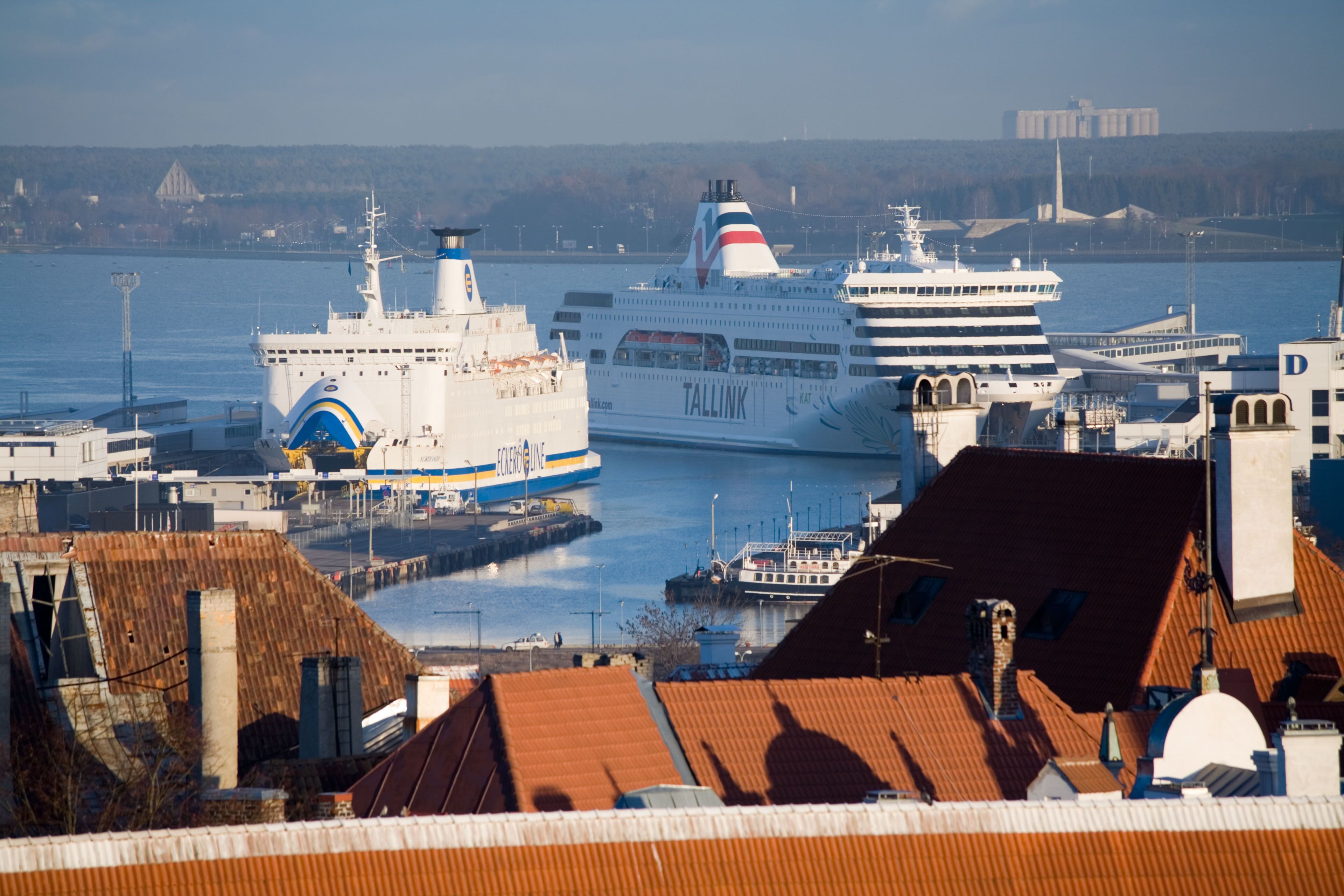 Un puerto con un gran crucero llamado 'Tallink' atracado, rodeado de edificios y un cielo despejado.