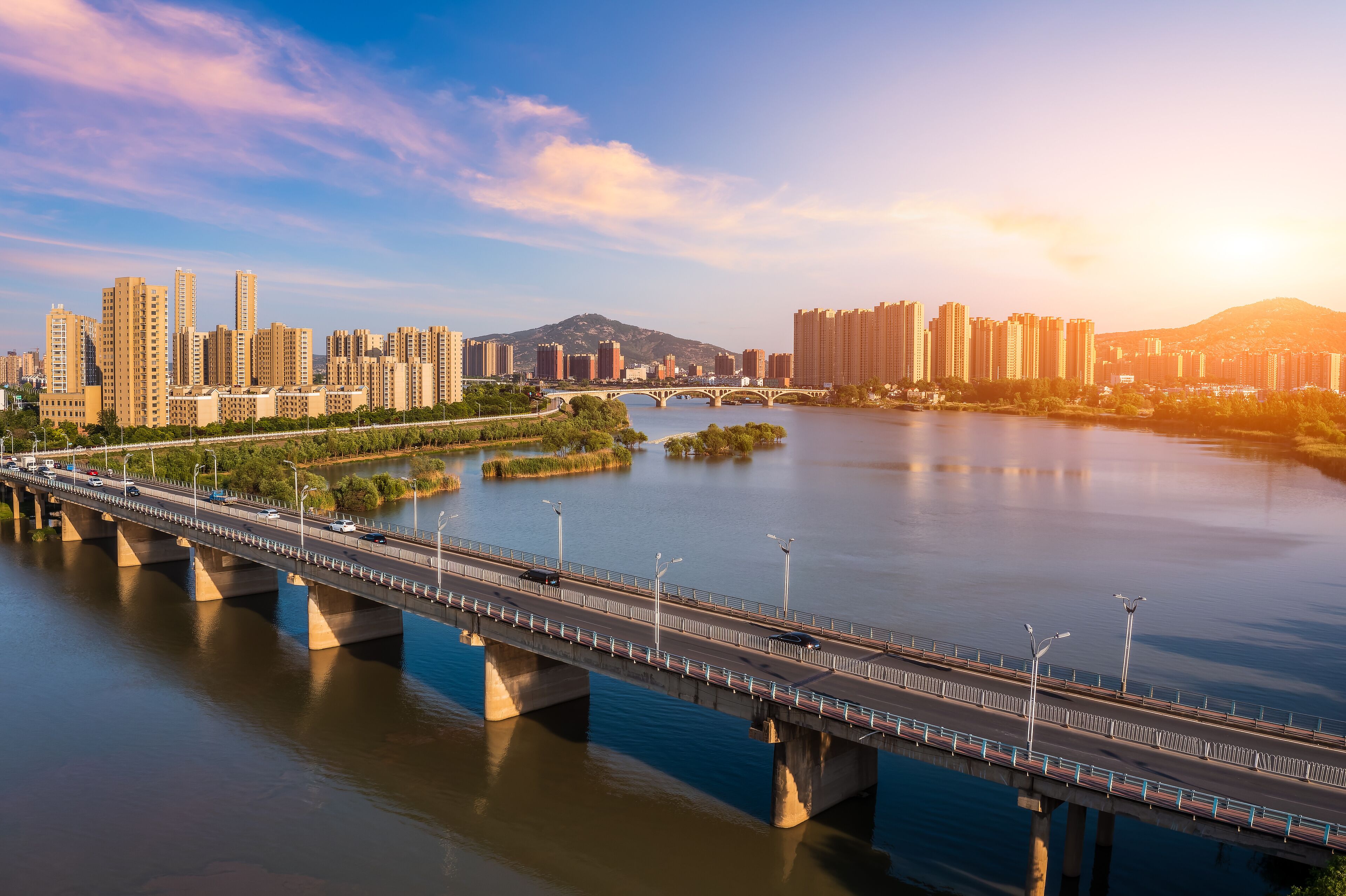 A river with a bridge, city skyline, and mountains in the background.