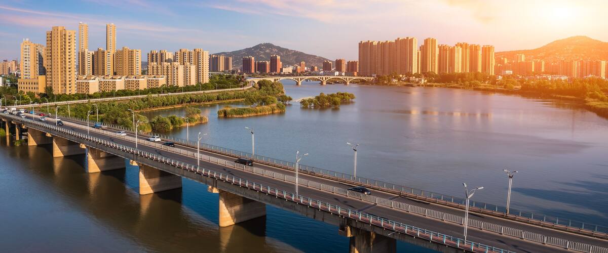A river with a bridge, city skyline, and mountains in the background.