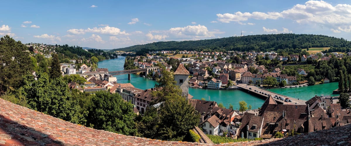 A town with a river, historic buildings, and a hill in the background.