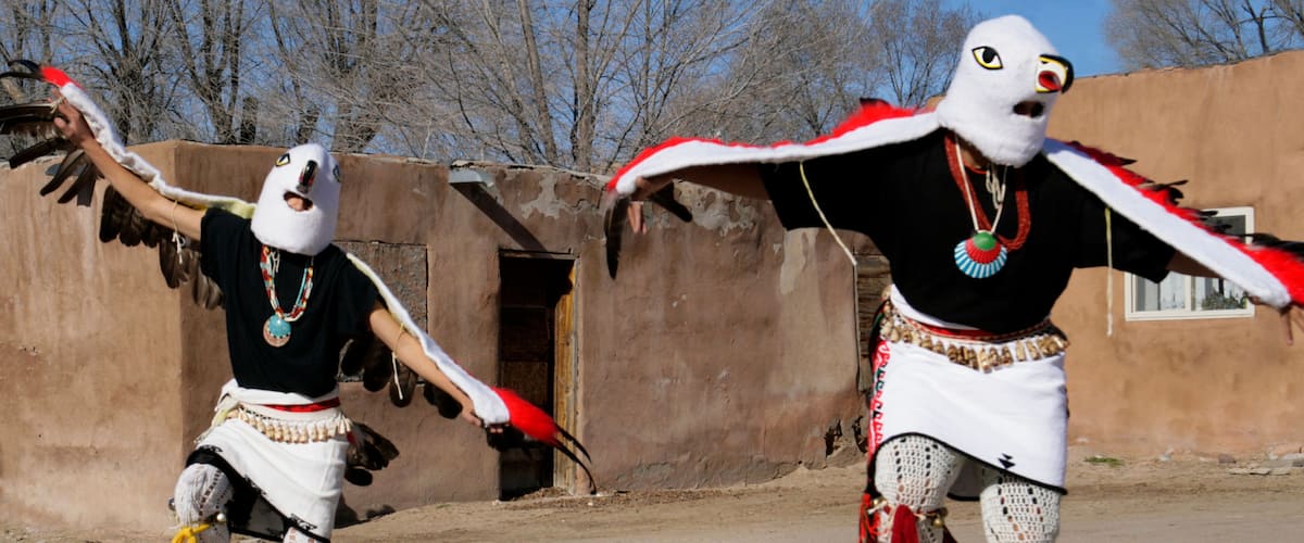 Two performers in traditional dance costumes with wings, performing in an outdoor setting with a building in the background.