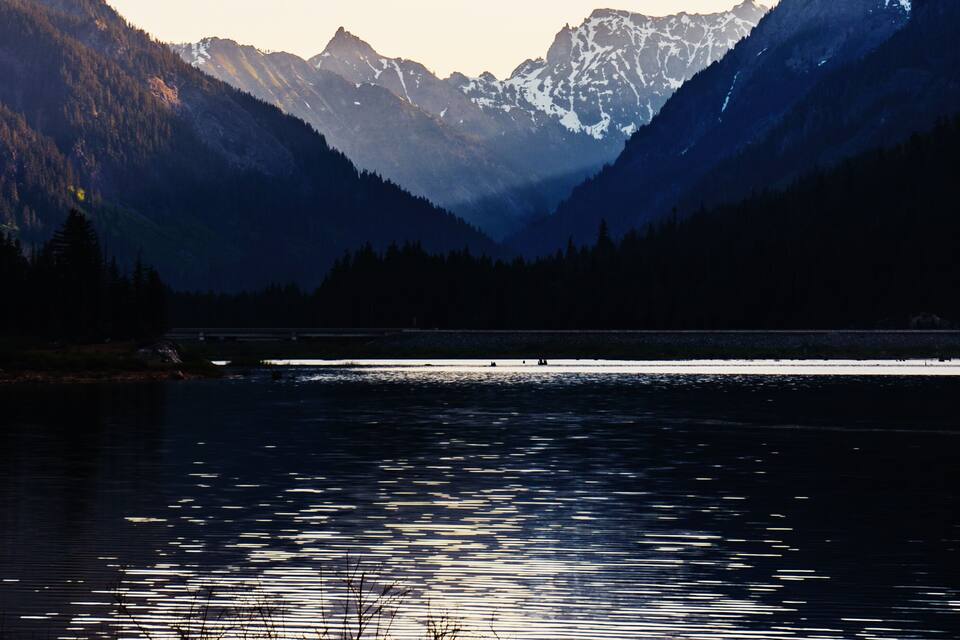 Una cordillera con picos nevados, un lago tranquilo y colinas cubiertas de bosques densos.