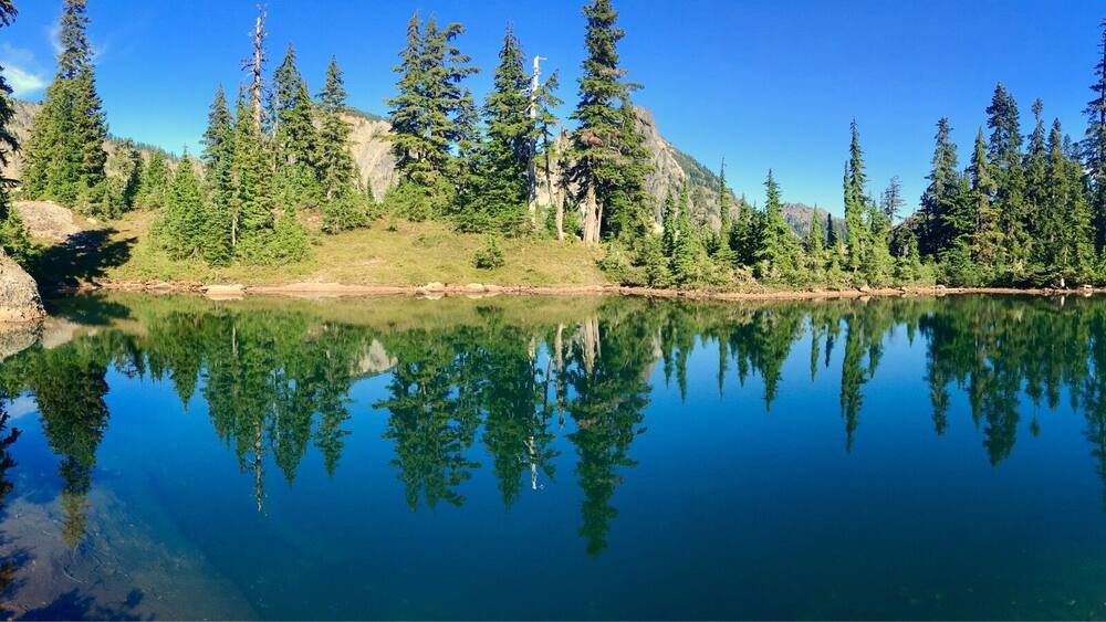Un lac aux eaux limpides, entouré d’une forêt dense et d’un paysage rocheux.